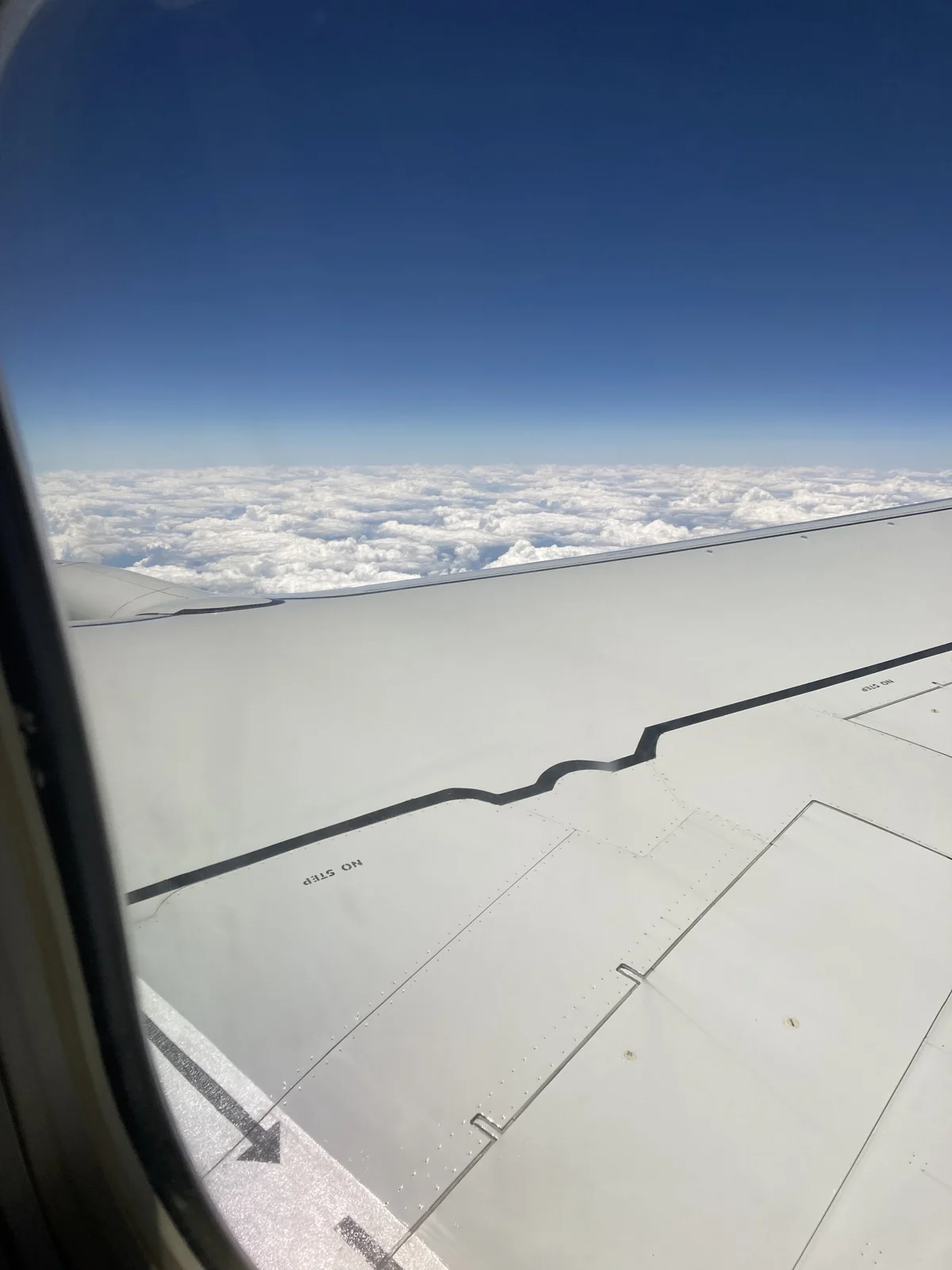 Airplane wing viewed through a window above white clouds